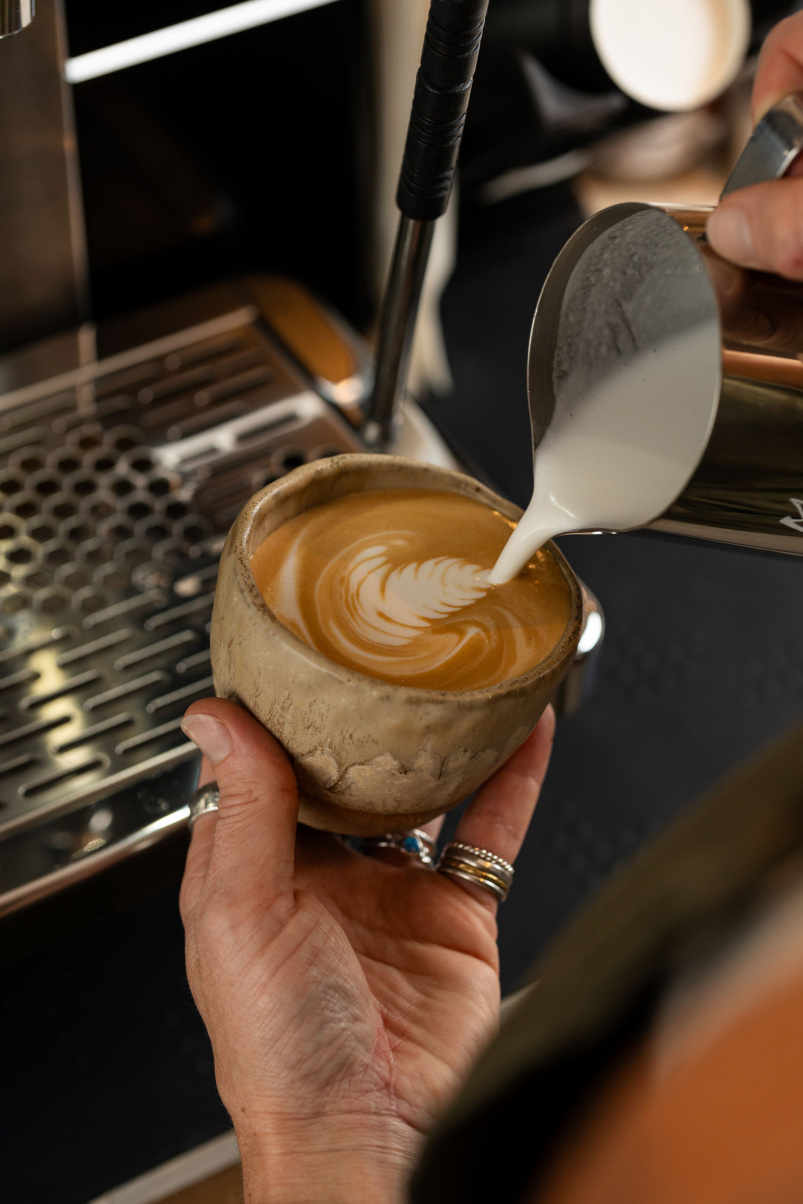 A flat white being poured into a rustic ceramic cup at the ELEMENTS café espresso bar in St Ives